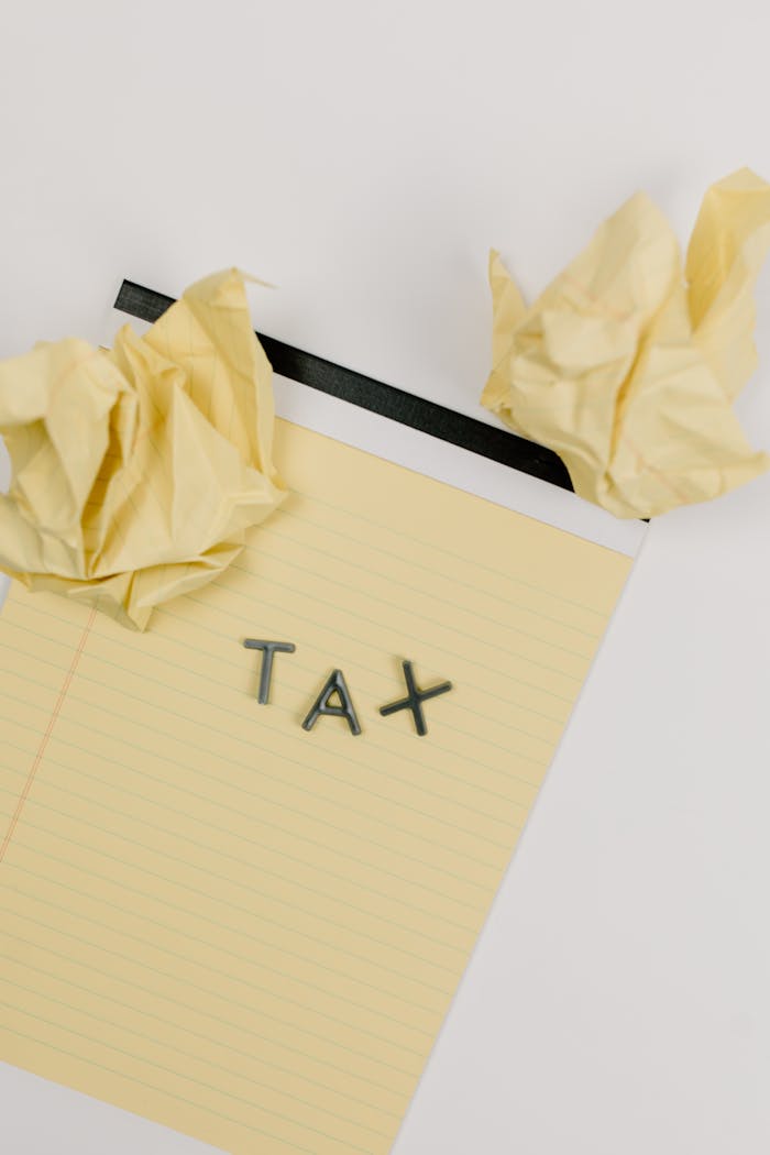 Yellow notepad featuring the word 'TAX' with crumpled paper, symbolizing taxation and paperwork frustration.